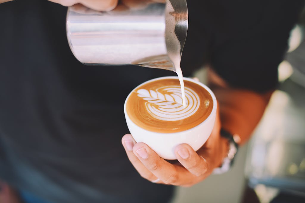 Close-up of a barista pouring latte art into a coffee cup indoors.